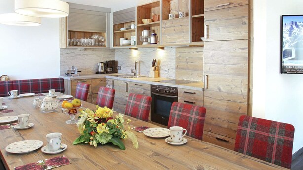Eine moderne Küche mit Holzschränken, einem Esstisch gedeckt mit Teetassen und Tellern, und einem großen floralen Arrangement.