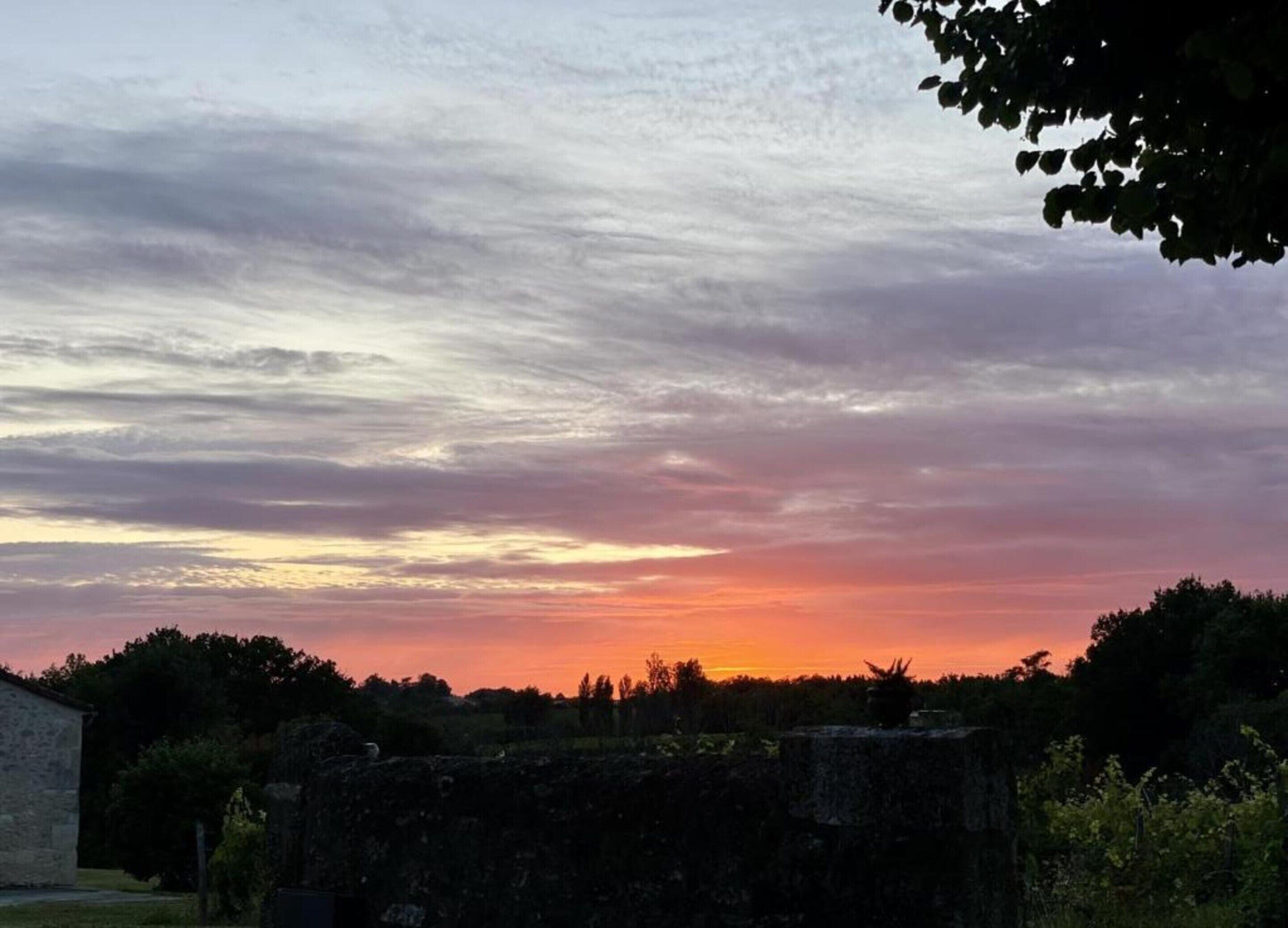 A sunset over a rural landscape with a stone wall and trees.