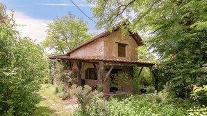 A rustic stone house with a wooden porch, surrounded by lush greenery and a garden path. - Cottage in Vezere Valley Near Lascaux Caves (Les Eyzies)