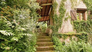 A stone staircase leading to a wooden structure with a window, surrounded by lush greenery. - Cottage in Vezere Valley Near Lascaux Caves (Les Eyzies)