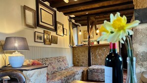 A cozy room with a wooden table, a sofa, and a lamp. There are framed pictures on the wall and a bottle of wine on the table. - Cottage in Vezere Valley Near Lascaux Caves (Les Eyzies)
