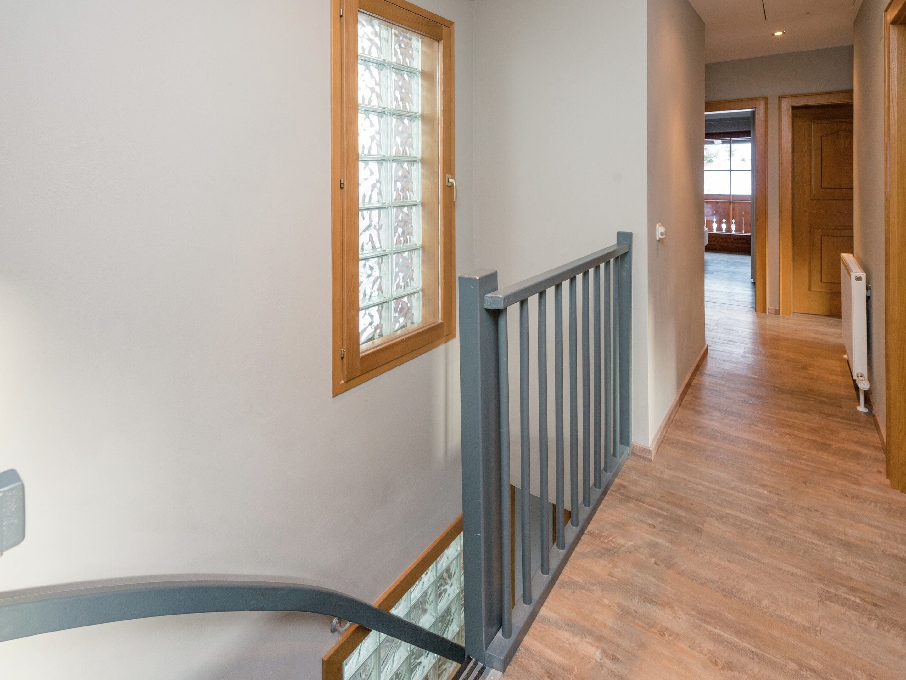 A hallway with a wooden floor, a glass door with a wooden frame, and a grey metal railing.