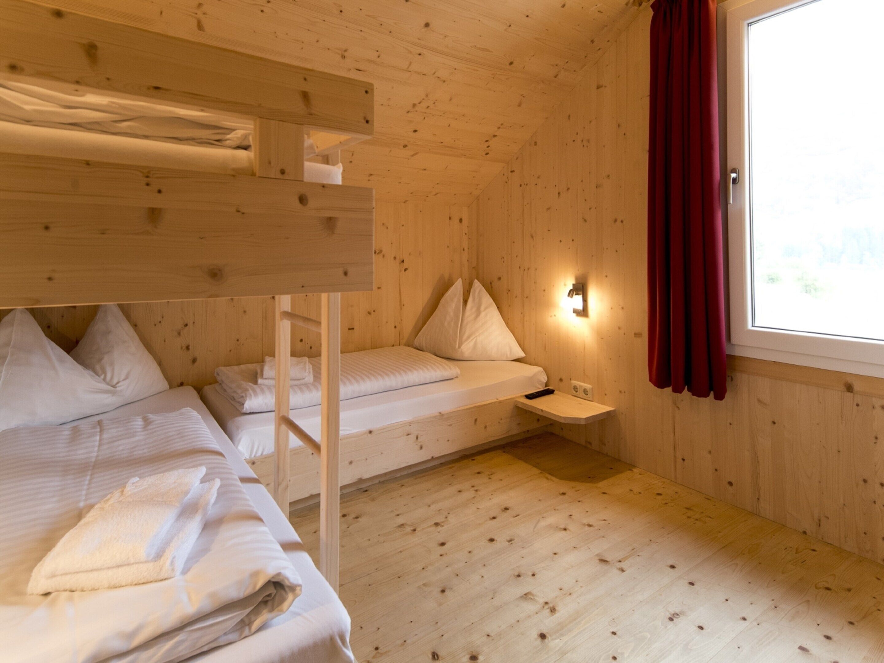 Una habitación de cabaña de madera con literas, una mesita de noche pequeña y una ventana con cortinas.