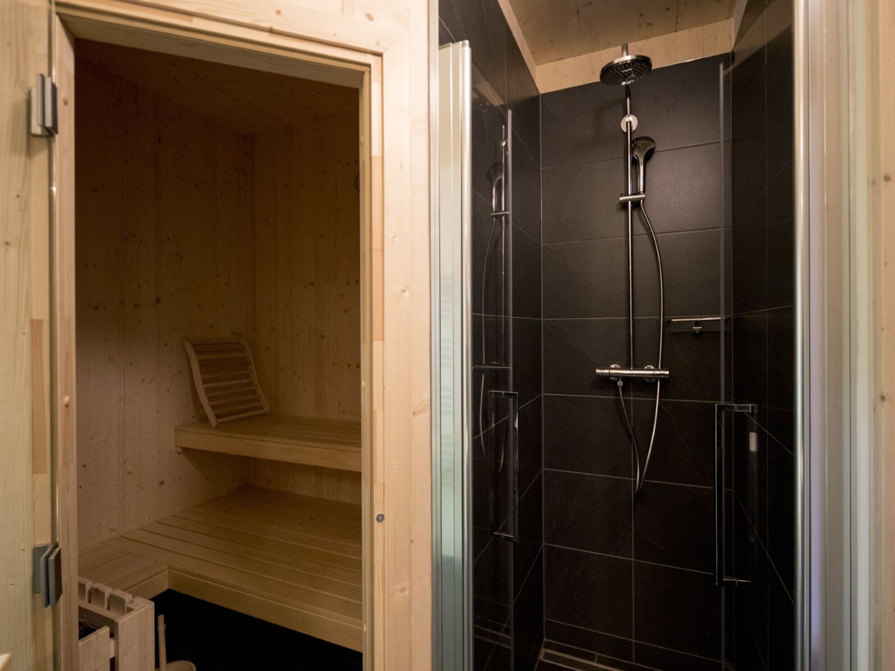 Eine Sauna mit einer Holzbank und einem separaten Duschbereich mit schwarzen Fliesen.