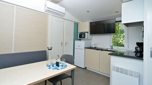 Eine kompakte Küche mit Essbereich, inklusive Tisch mit Stühlen, einer Mikrowelle, einem Kühlschrank und einem Fenster mit Blick auf Grünflächen.