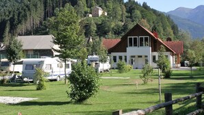 Ein zweigeschossiges Gebäude mit rotem Dach, umgeben von einer Rasenfläche mit Bäumen und einem Berg im Hintergrund.