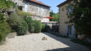 Un bâtiment en pierre avec un toit recouvert de tuiles rouges, une cour en gravier et un parasol rouge.