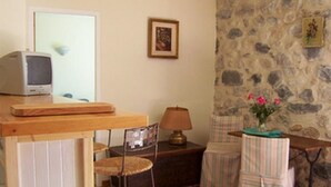 Une pièce chaleureuse avec un mur en pierre, une table en bois sur laquelle se trouvent une télévision et une lampe, ainsi qu’un petit tabouret.