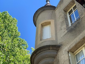 Un coin d’un bâtiment, avec un élément architectural arrondi, une fenêtre et un arbre.