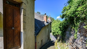A narrow alleyway with a stone wall on one side and a building with a wooden door on the other.