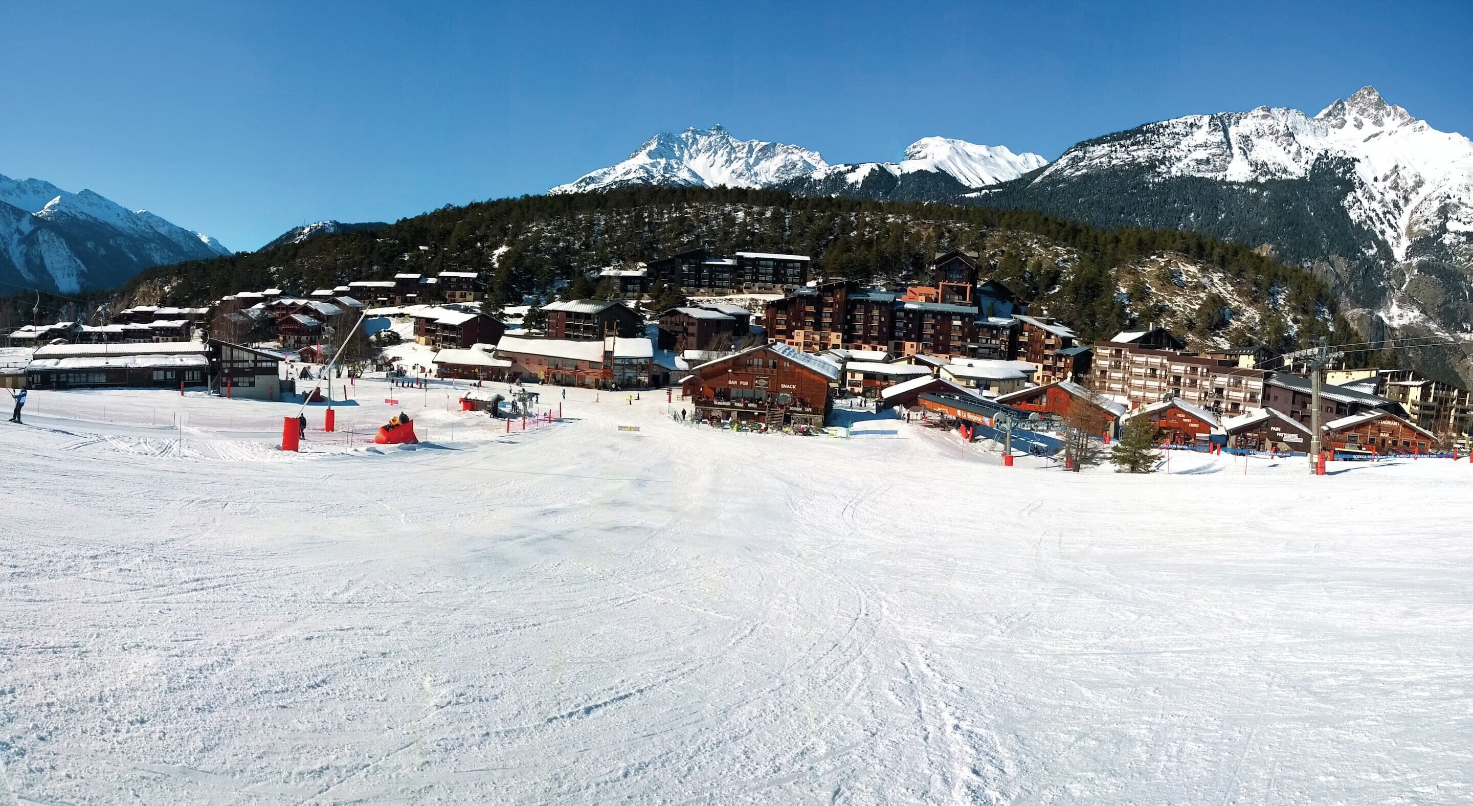 A snow-covered ski resort with buildings, a bar, and a mountain backdrop.