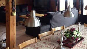 Ein gemütliches Wohnzimmer mit Holzbalken, einer Couch, einem Fernseher und hängenden Pendelleuchten.