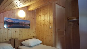 Ein Zimmer mit Holzboden, einem Bett, einer Wandleuchte und einem Bild von einer Berglandschaft.