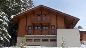 Eine Holzchalet mit einem Balkon, umgeben von schneebedeckten Bäumen.