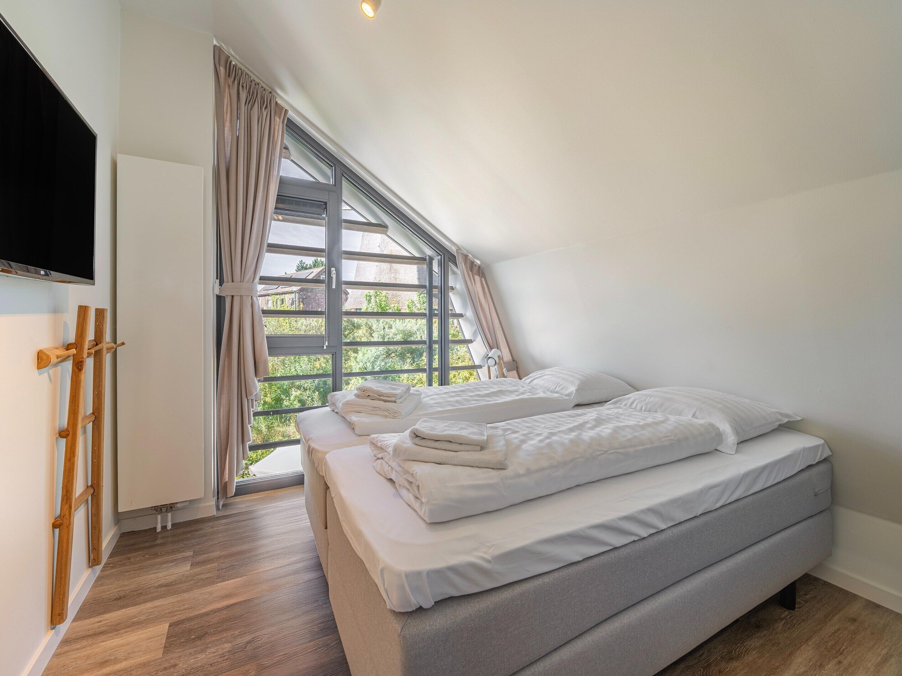 A bedroom with two beds, a large window, and a wooden floor.
