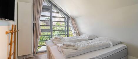 A bedroom with two beds, a large window, and a wooden floor.