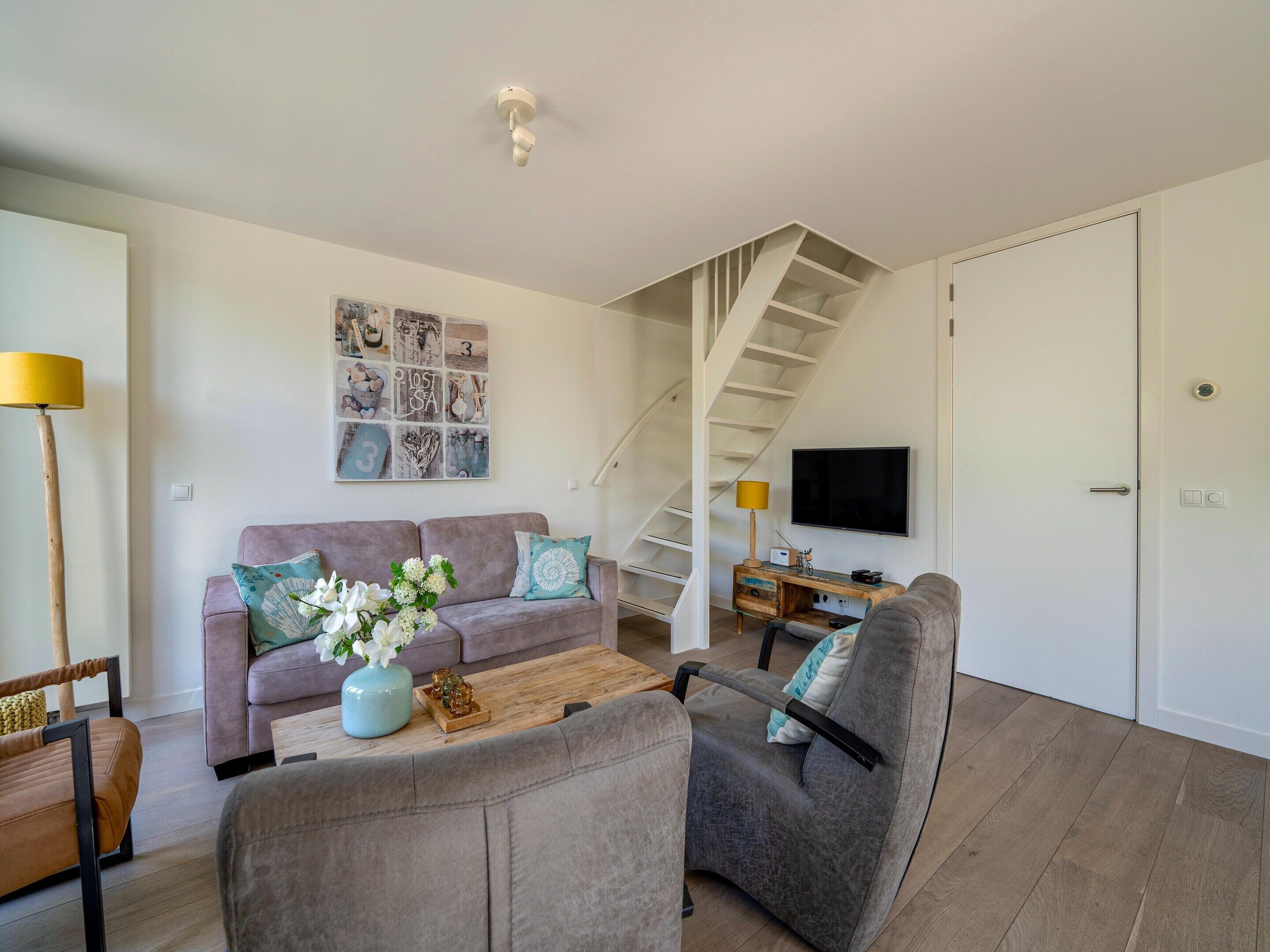 Un salon moderne avec un canapé, des fauteuils, une table basse et un escalier.
