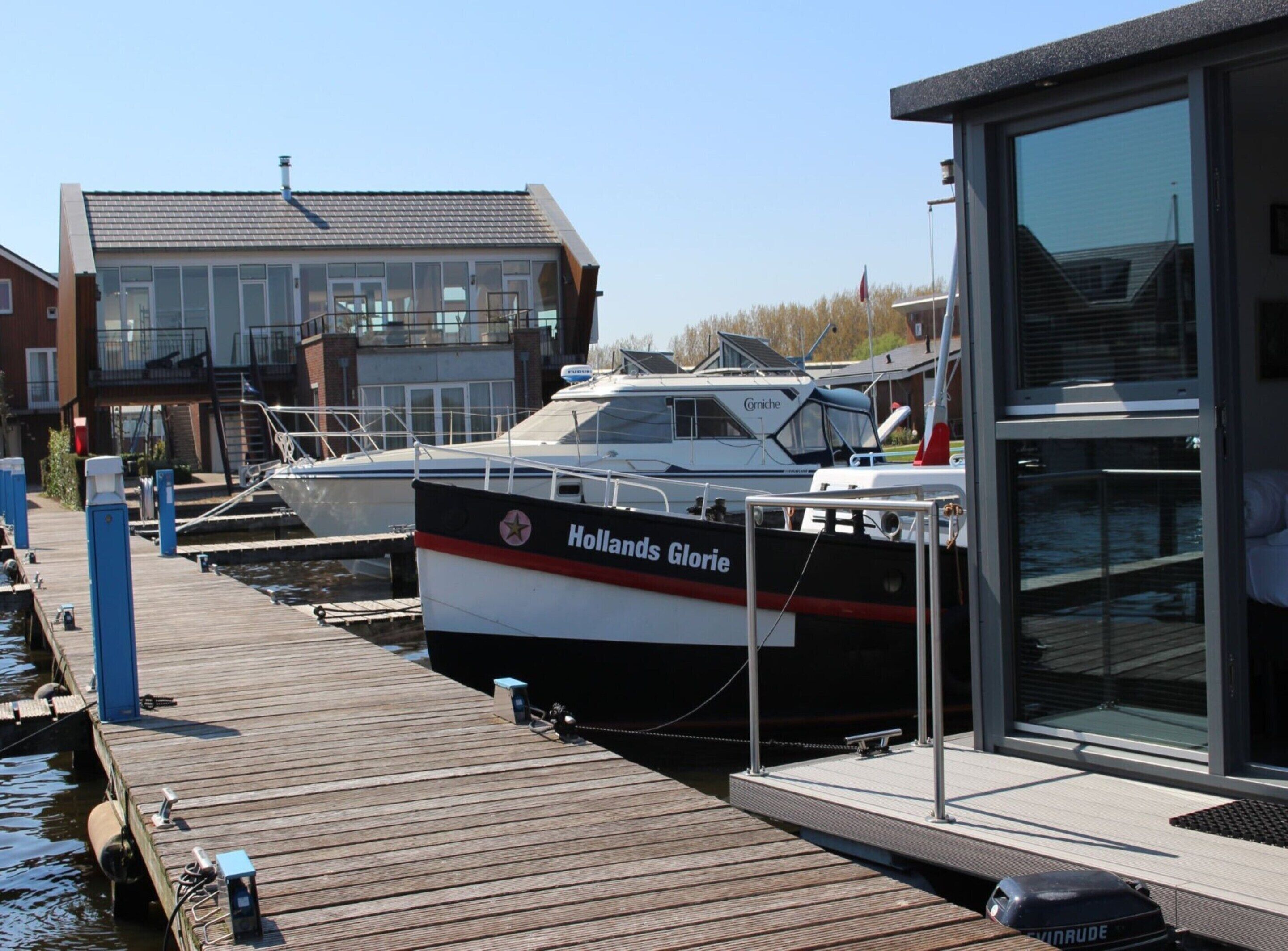 A dock with a boat named 'Holland's Glory' moored alongside a building with a glass facade.