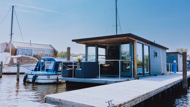 Un quai moderne doté d’une structure fermée par des parois de verre, un bateau et un bâtiment en arrière-plan.