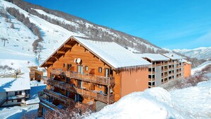 Un chalet en bois doté de balcons, un télésiège en arrière-plan et un paysage montagneux enneigé.