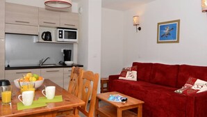 Un espace de vie compact comprenant un coin cuisine, un coin repas avec une table et des chaises, un canapé rouge et une petite table d’appoint.