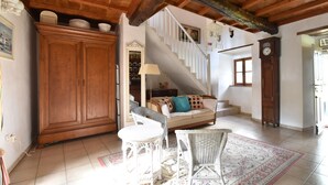 Un amplio salón con techos altos, una escalera, un armario de madera, un sofá con cojines y una mesa de comedor.