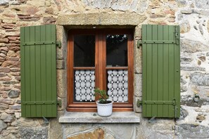 A stone building with a window featuring green shutters, a lace curtain, and a potted plant. - Saint-sauveur Hideaway (Saint-Sauveur-Villages)