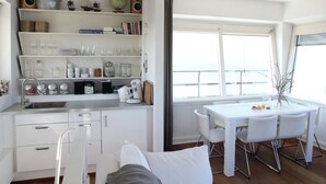Una cocina moderna con armarios blancos, una zona de comedor con una mesa y sillas blancas, y un ventanal que ofrece vistas al exterior.