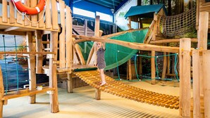 Eine Holzspielkonstruktion mit einer Seilbrücke, einem Kletterbereich mit Netz und einem Rettungsring.