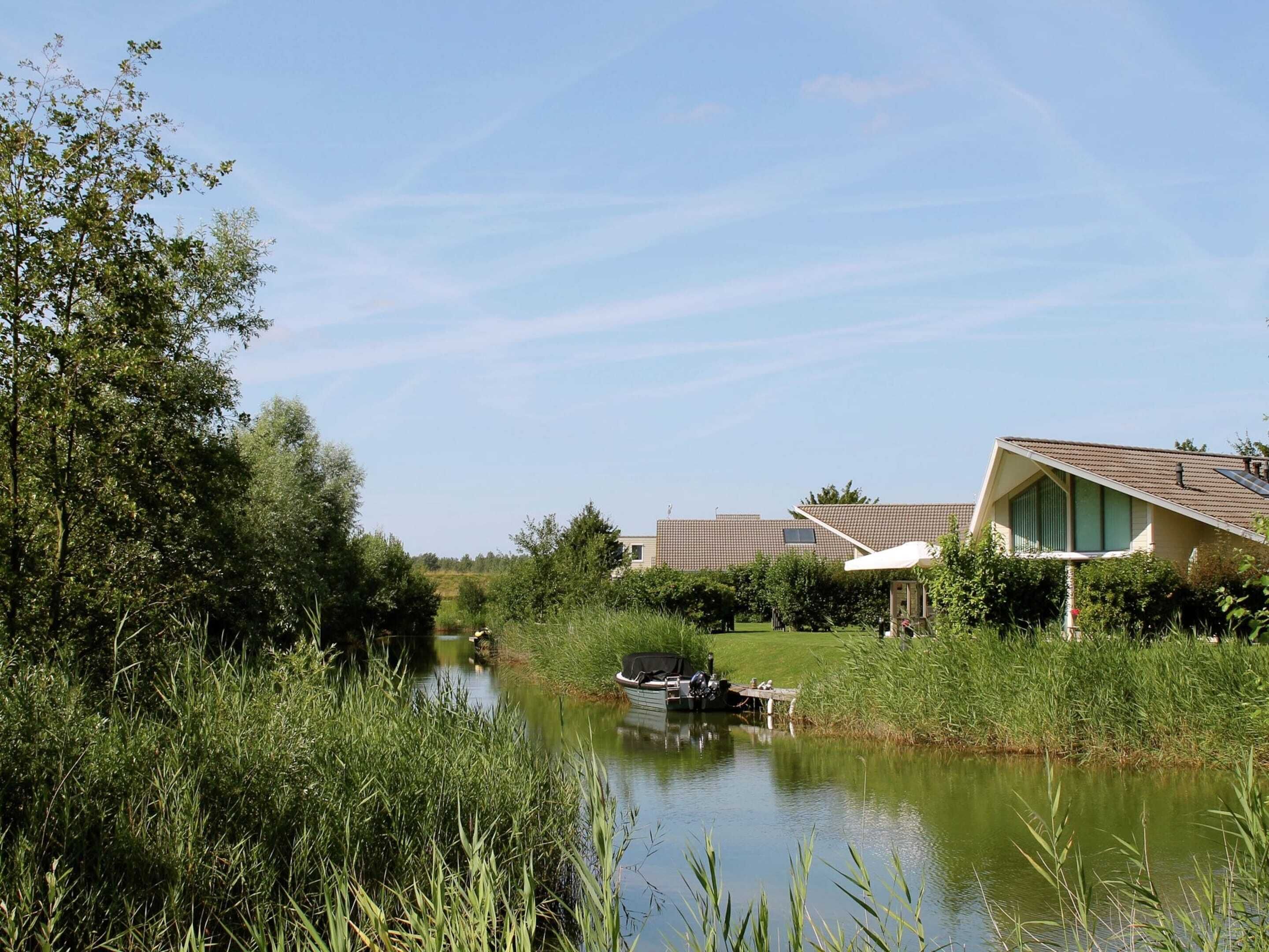 A riverside view with a boat docked near a building with a sloped roof and a small deck.