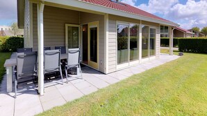 Ein einstöckiges Haus mit einer überdachten Terrasse, Schiebegläsern und einem roten Ziegeldach.