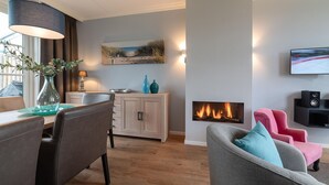 A modern living room with a fireplace, a dining area with a table and chairs, and a TV mounted on the wall. - Holiday Home in Colijnsplaat by the Lake (Colijnsplaat)