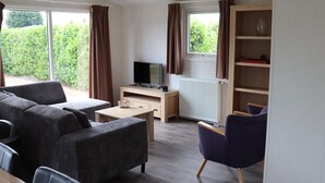 A modern living room with a sofa, a small table, a TV, and a bookshelf. - Chalet in Netherlands With Pool & Playground (Udenhout)