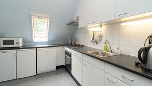 Une cuisine avec des meubles blancs, un four à micro-ondes, un lave-vaisselle, un évier et une fenêtre.
