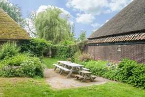A rustic outdoor area with a picnic table, a brick building, and a thatched-roof structure. - Inviting Farmhouse in 't Zand near Marine Museum (t Zand)
