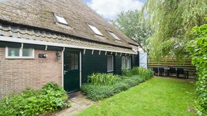 Une maison traditionnelle avec un toit en pente, une porte verte et un petit jardin avec une pelouse et une table entourée de chaises.