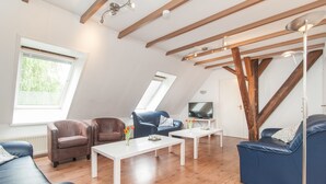 Un appartement moderne de style « loft », avec des poutres apparentes, une grande verrière, un téléviseur à écran plat et un coin salon confortable agrémenté de canapés et de fauteuils en cuir.