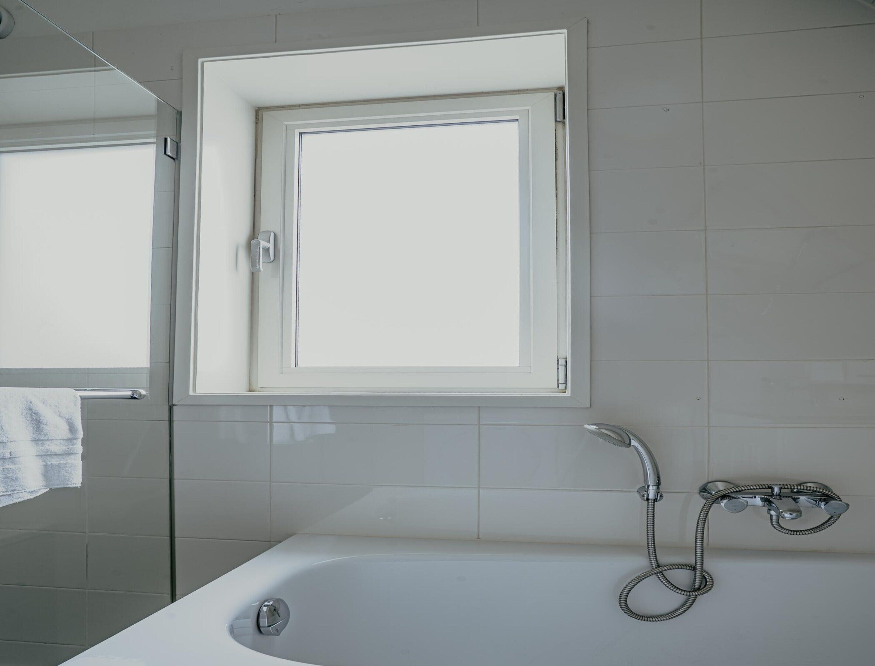 A bathroom with a bathtub, a shower, and a window above the bathtub.