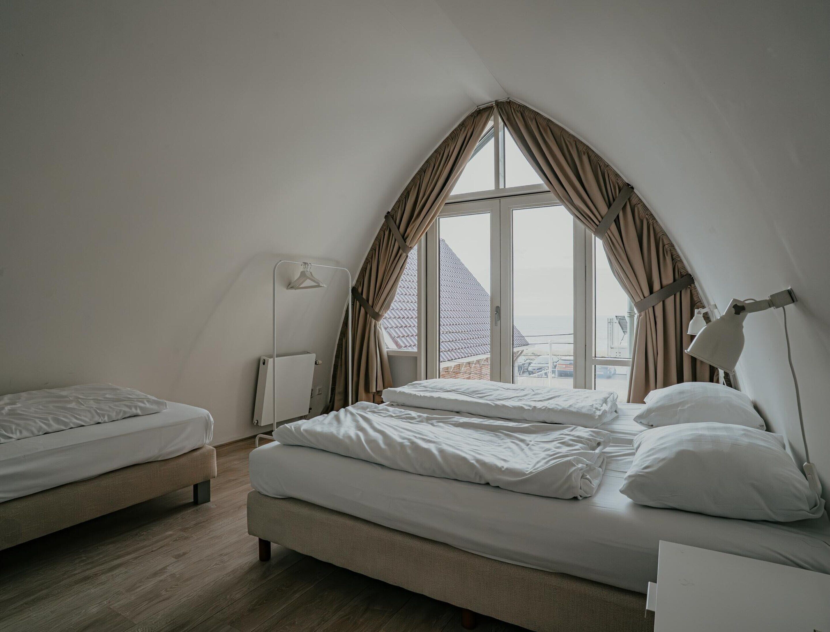 A bedroom with a large window, a bed, a bedside table, and a lamp.