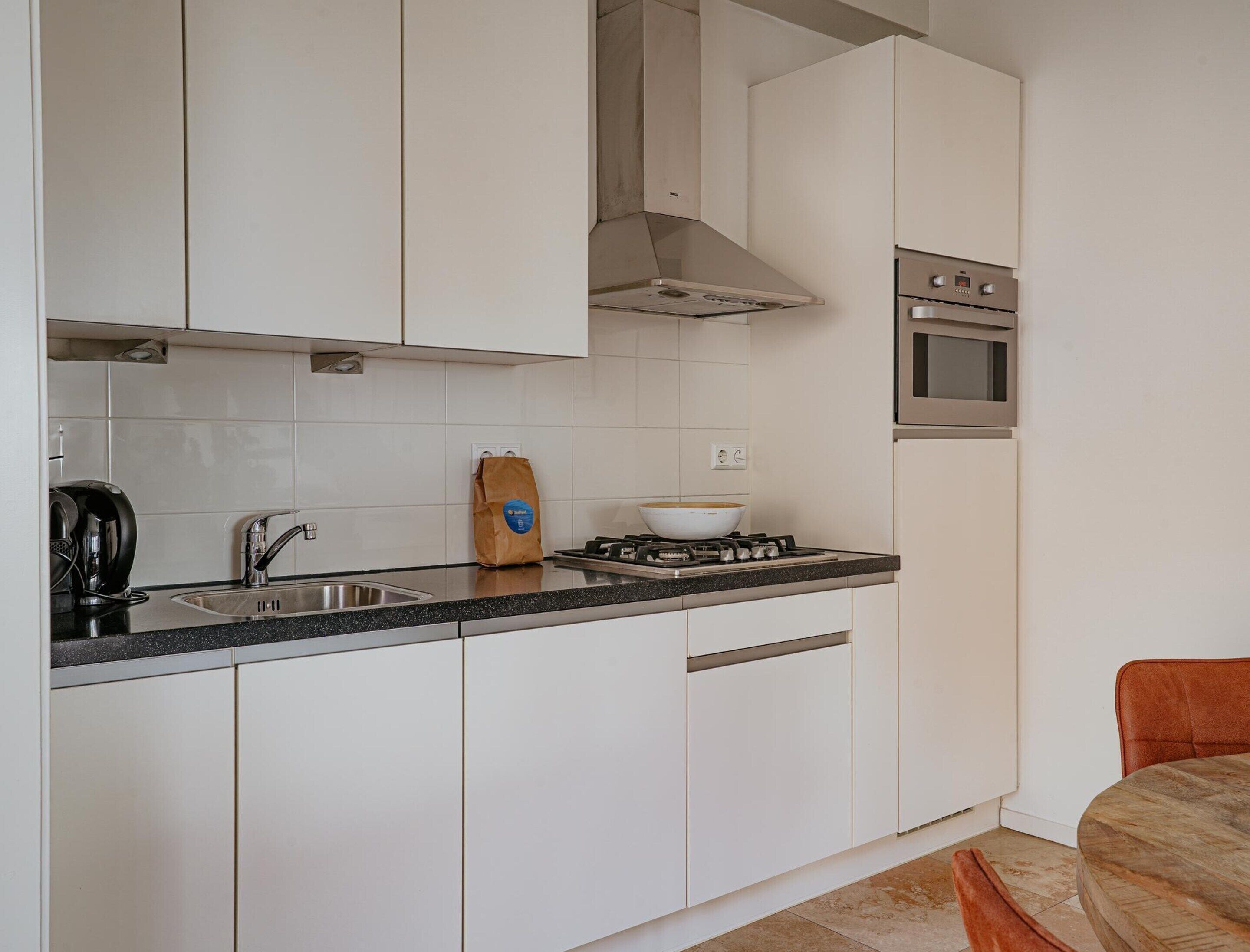 Une cuisine moderne avec des meubles blancs, une cuisinière à gaz, un four et un évier.