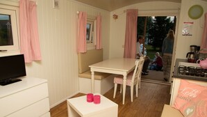 A compact, well-lit room with a television, a small table, and a bench. - Living Van on the Beach With Sea Views ('s-Gravenzande)