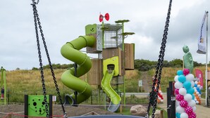 A playground with a green spiral slide, a swing set, and a decorative archway. - Living Van on the Beach With Sea Views ('s-Gravenzande)
