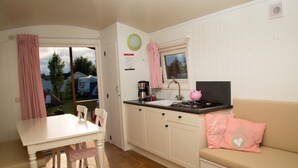 A compact kitchenette with a stove, sink, and a small window. There is a dining table with chairs and a sofa with a heart-patterned pillow. - Living Van on the Beach With Sea Views ('s-Gravenzande)