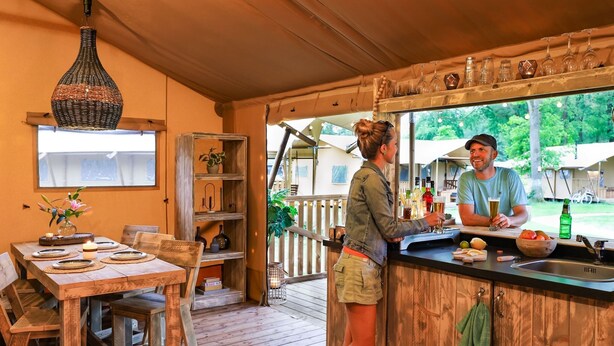 Une cuisine rustique avec un comptoir en bois, un luminaire suspendu et un coin repas avec une table dressée pour quatre personnes.