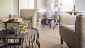 A modern living room with a round coffee table, two armchairs, and a dining area with chairs and a table. - Apartment in De Cocksdorp With Garden (De Cocksdorp)