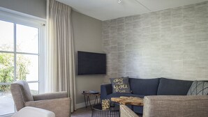 A modern living room with a grey sofa, two armchairs, a coffee table, and a flat-screen TV mounted on the wall. - Apartment in De Cocksdorp With Garden (De Cocksdorp)