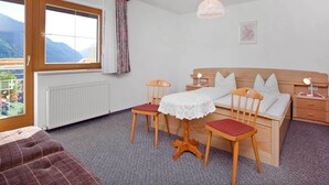 A bedroom with a wooden bed, a table with chairs, a window with a view of mountains, and a radiator. - Apartment Near the Lake in Tyrol (Kappl)