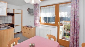 A kitchen with a dining table, wooden cabinets, a built-in oven, and a window with curtains. - Apartment Near the Lake in Tyrol (Kappl)