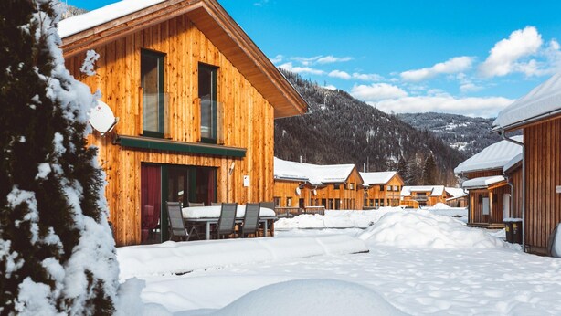Uma cabana de madeira com vários quartos, uma área de estar coberta ao ar livre e montanhas nevadas ao fundo.