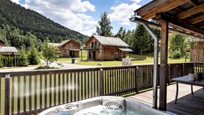 A hot tub on a wooden deck with a view of cabins in a forested area. - Appealing Chalet With Terrace (Stadl-Predlitz)